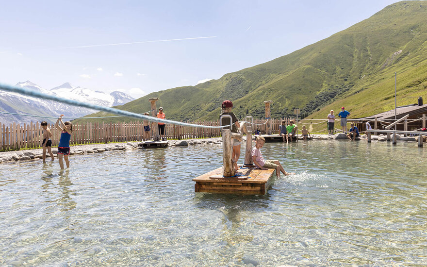 Kinder spielen fröhlich im Wasser, während die Berge im Hintergrund eine malerische Kulisse bieten.