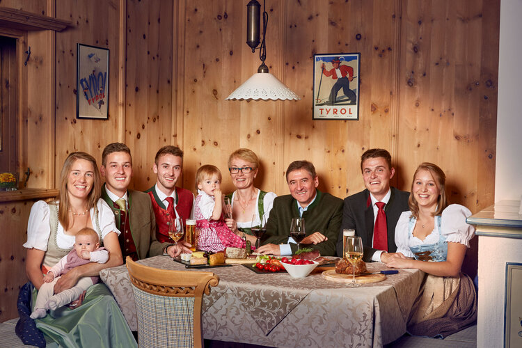 Eine fröhliche Familie sitzt um einen Tisch, umgeben von traditioneller Tiroler Dekoration und köstlichem Essen.