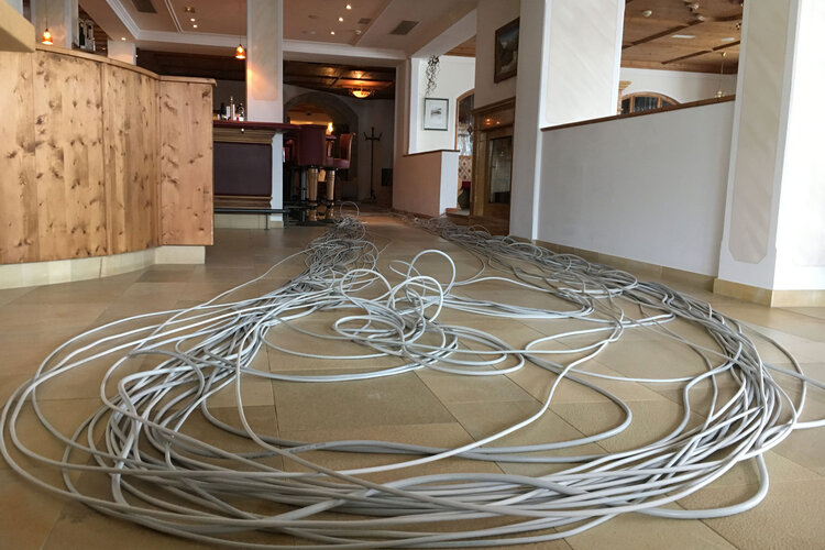 Ein langer Kabelstrang liegt unordentlich auf dem Boden eines eleganten Innenraums mit Holzdetails und sanfter Beleuchtung.