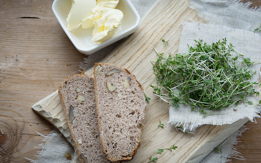 Auf einem rustikalen Holzbrett sind zwei Scheiben Brot, frische Kräuter und eine kleine Schale mit Butter arrangiert.