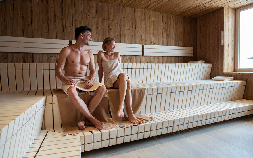 Ein Paar sitzt entspannt in einer modernen Sauna, umgeben von Holzverkleidung und hellen Bänken.
