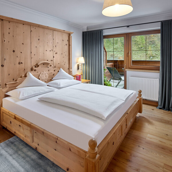 Ein gemütliches Schlafzimmer mit einem großen Holzbett, weißen Kissen und einer warmen Holzverkleidung an der Wand.