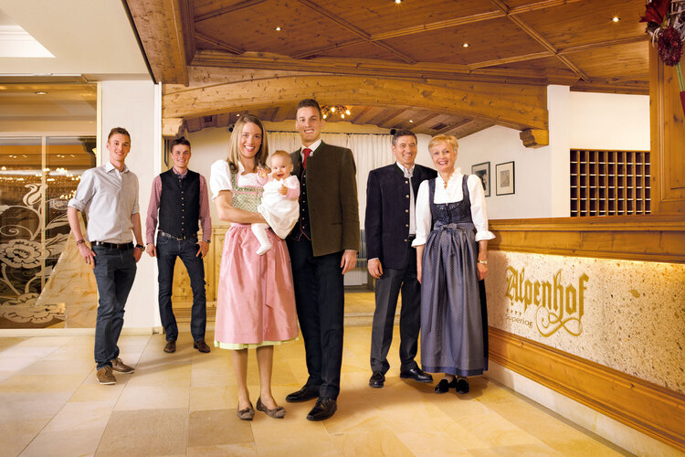 Im Alpenhof posiert eine Familie in Trachten, umgeben von einem eleganten, rustikalen Interieur und warmem Licht.
