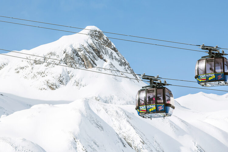 Zwei moderne Gondeln schweben über schneebedeckte Berge unter einem strahlend blauen Himmel, ideal für Wintersportler.