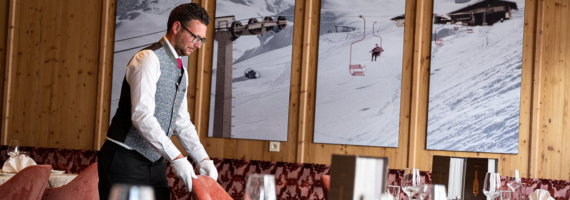 Der Oberkellner im Hotel Alpenhof stellt den Stuhl an seinen Platz zum gedeckten Tisch.
