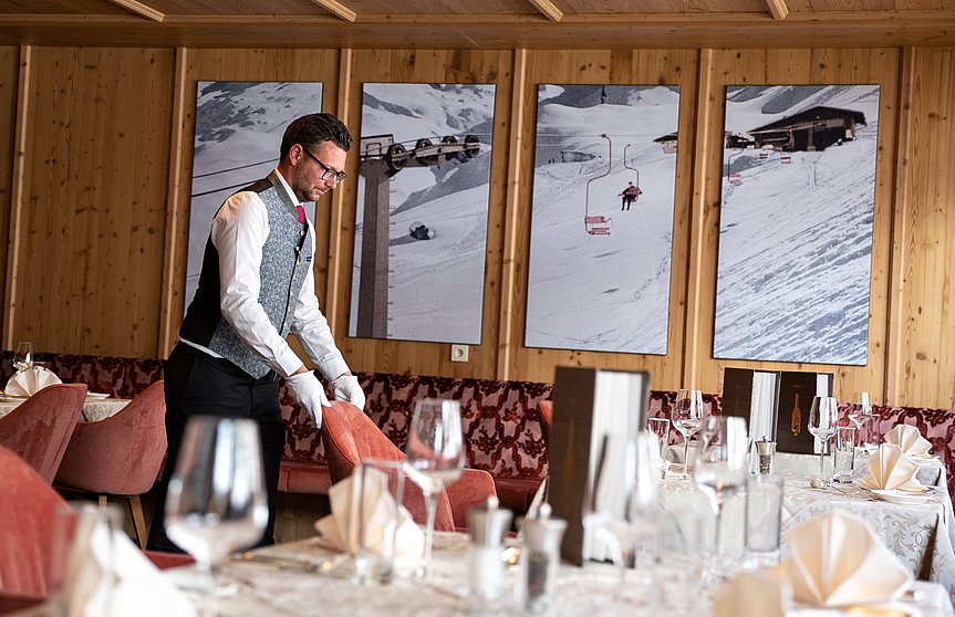 Der Oberkellner im Hotel Alpenhof stellt den Stuhl an seinen Platz zum gedeckten Tisch.