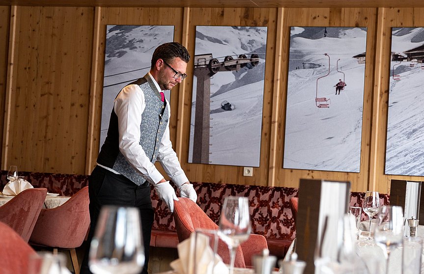 Der Oberkellner im Hotel Alpenhof stellt den Stuhl an seinen Platz zum gedeckten Tisch.