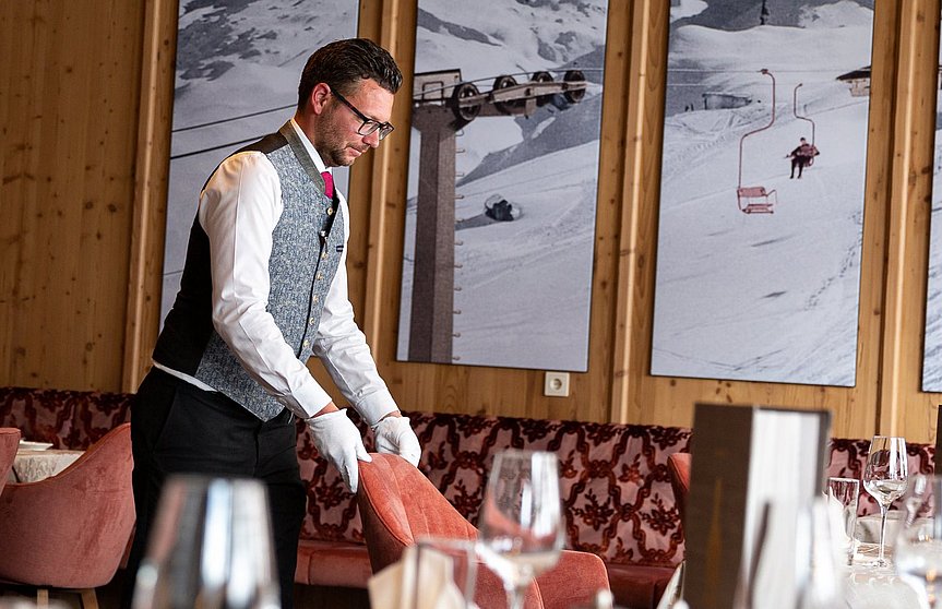 Der Oberkellner im Hotel Alpenhof stellt den Stuhl an seinen Platz zum gedeckten Tisch.