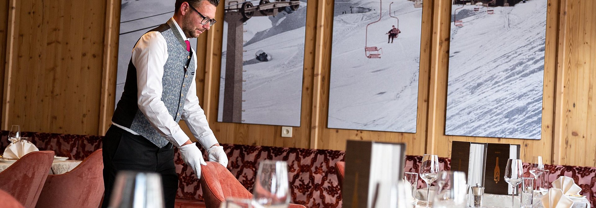Der Oberkellner im Hotel Alpenhof stellt den Stuhl an seinen Platz zum gedeckten Tisch.
