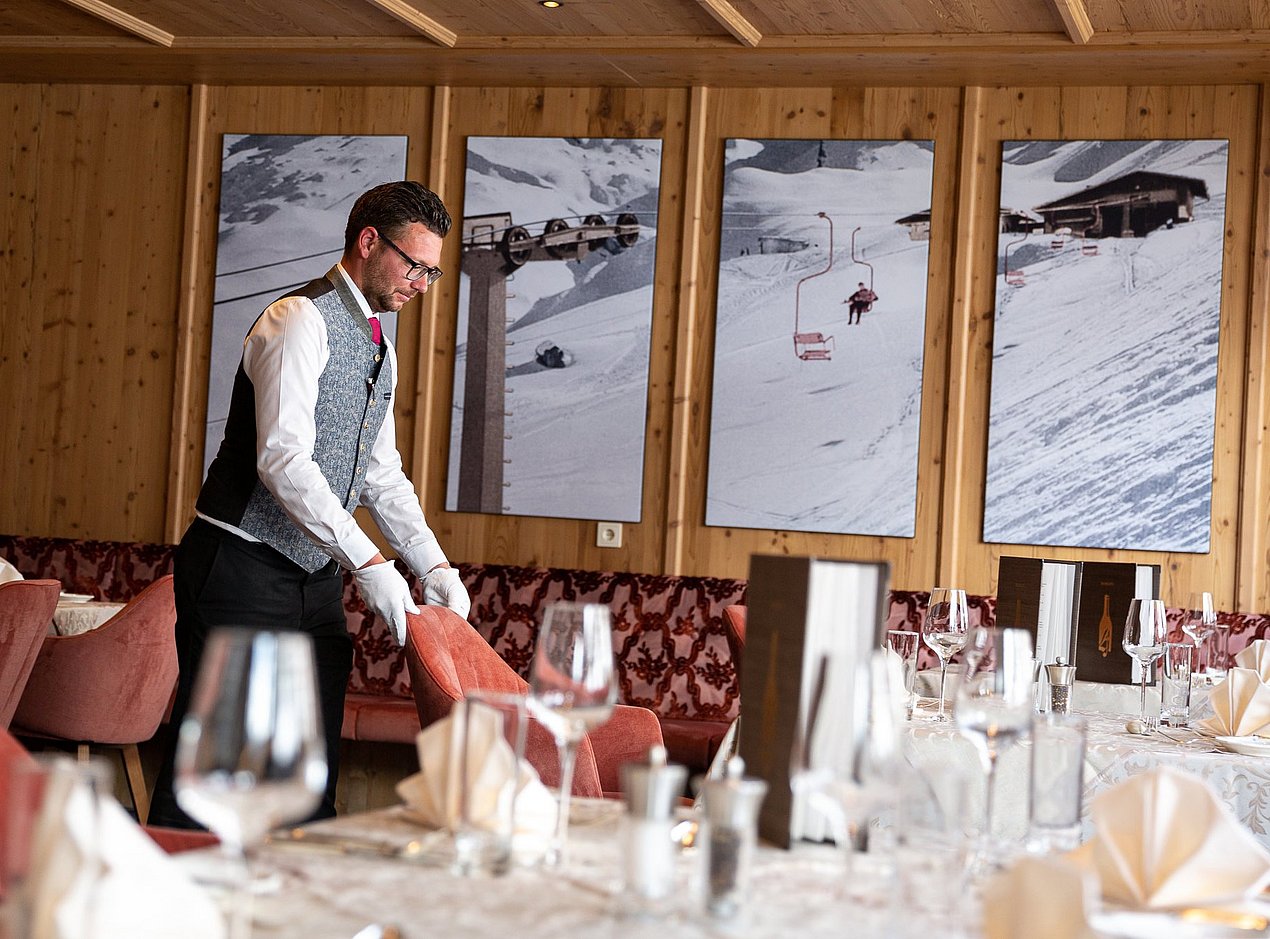 Der Oberkellner im Hotel Alpenhof stellt den Stuhl an seinen Platz zum gedeckten Tisch.
