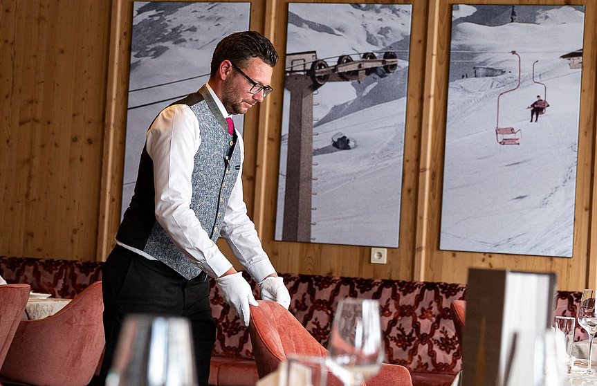 Der Oberkellner im Hotel Alpenhof stellt den Stuhl an seinen Platz zum gedeckten Tisch.