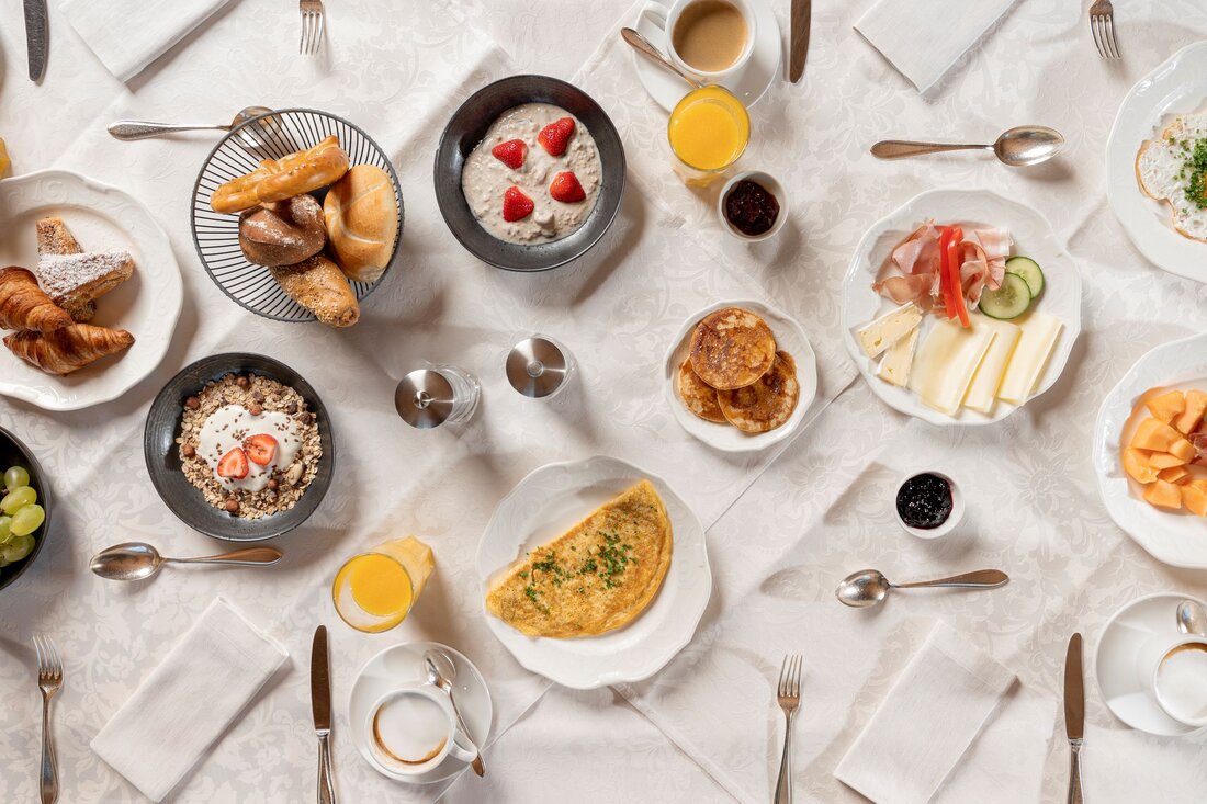 Ein reichhaltiges Frühstücksbuffet mit frischen Brötchen, Obst, Joghurt und einer Auswahl an Käse und Aufschnitt auf einem Tisch.