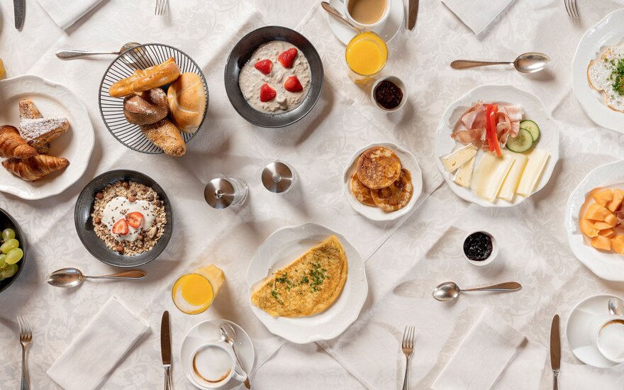 Ein reichhaltiges Frühstücksbuffet mit frischen Brötchen, Obst, Joghurt und einer Auswahl an Käse und Aufschnitt auf einem Tisch.