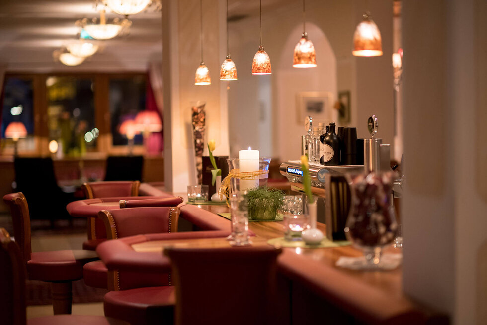 Eine stilvolle Hotelbar mit roten Polsterstühlen, sanfter Beleuchtung und einem einladenden Ambiente für entspannte Abende.