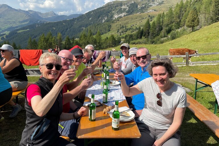 Freunde genießen ein geselliges Beisammensein im Freien, umgeben von grünen Wiesen und majestätischen Bergen.