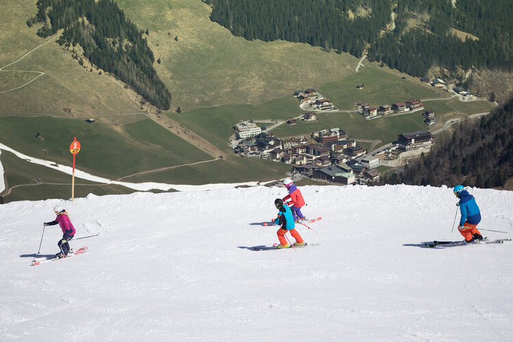 Eine Gruppe von Skifahrern fährt die Piste hinunter, umgeben von schneebedeckten Bergen und einer malerischen Landschaft.