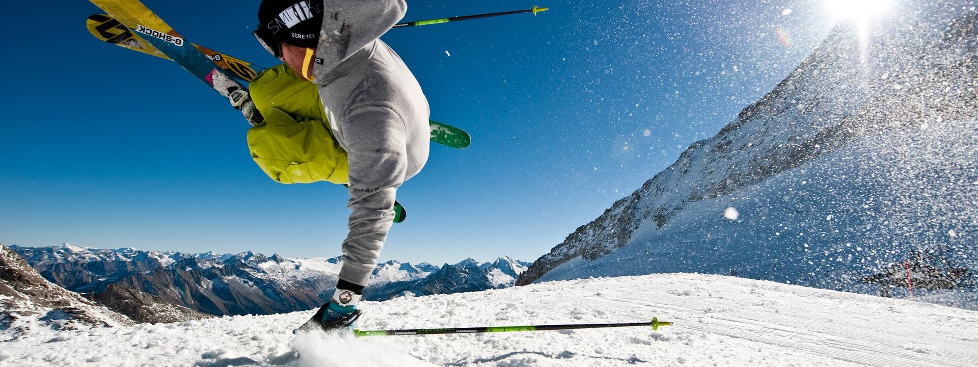 Ein Skifahrer führt einen beeindruckenden Sprung in den Zillertaler Alpen aus, umgeben von schneebedeckten Bergen und klarem Himmel.