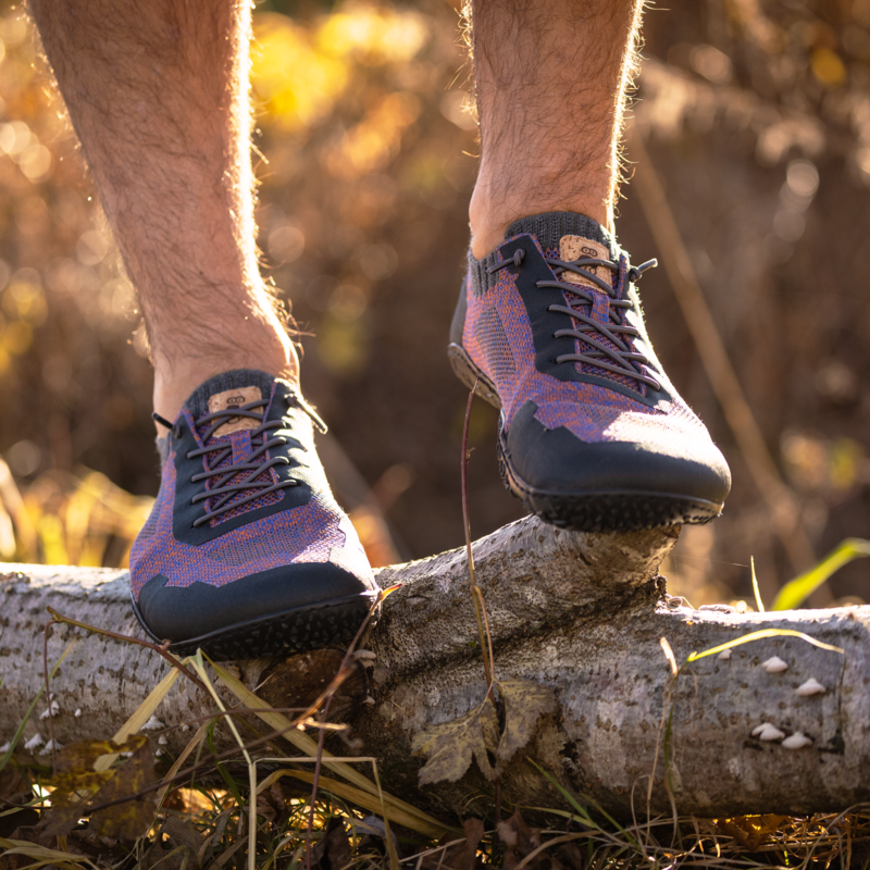 Ein Mann mit violetten Schuhen steht auf einem liegenden Baumstamm.
