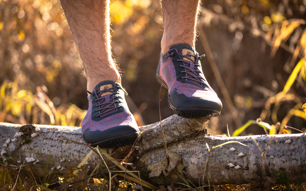 Ein Mann mit violetten Schuhen steht auf einem liegenden Baumstamm.