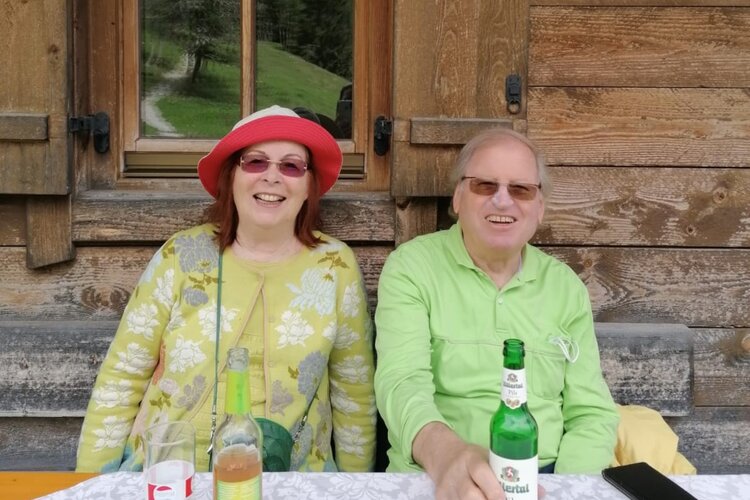 Ein fröhliches Paar sitzt an einem Tisch vor einer Holzwand, beide lächeln und genießen die Zeit zusammen in der Natur.