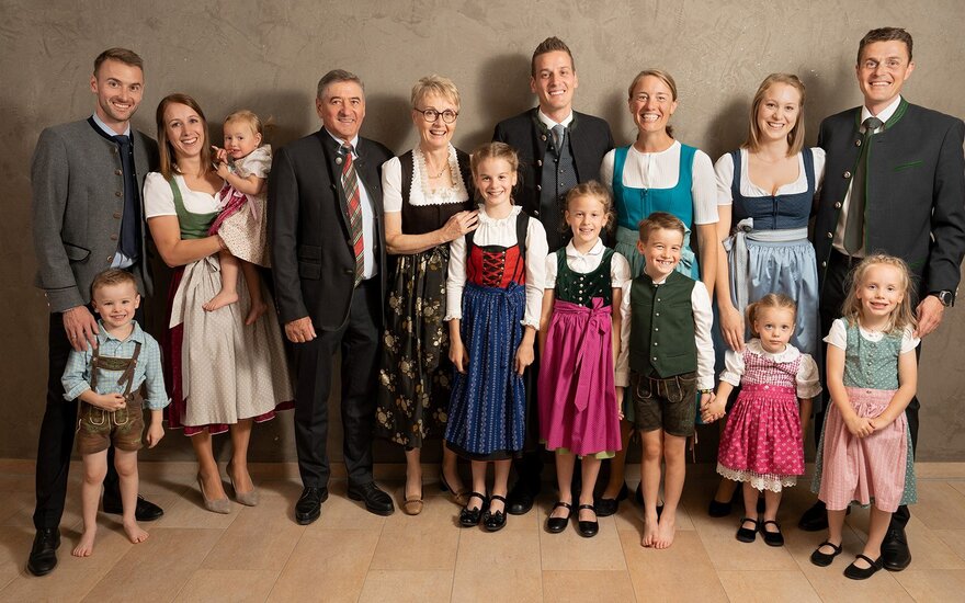 Eine große Familie in traditioneller Kleidung lächelt in die Kamera, während sie eine herzliche und festliche Atmosphäre ausstrahlt.