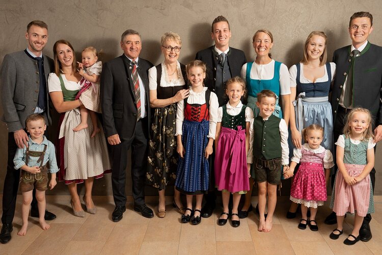 Eine große Familie in traditioneller Kleidung lächelt in die Kamera, während sie eine herzliche und festliche Atmosphäre ausstrahlt.