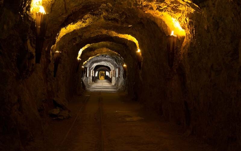 Der Tunnel eines Bergwerks, erhellt von warmem Licht, das die rauen Felsen und den schmalen Weg betont.