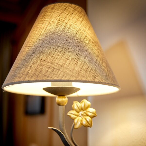 Eine elegante Lampe mit einem goldenen Blumenmotiv und einem schlichten Lampenschirm, der warmes Licht ausstrahlt.