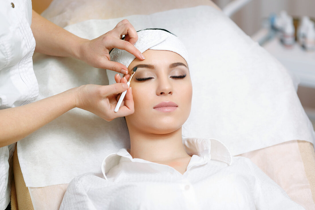 Eine Frau liegt entspannt auf einer Liege, während ihre Augenbrauen von einer Kosmetikerin geformt werden.