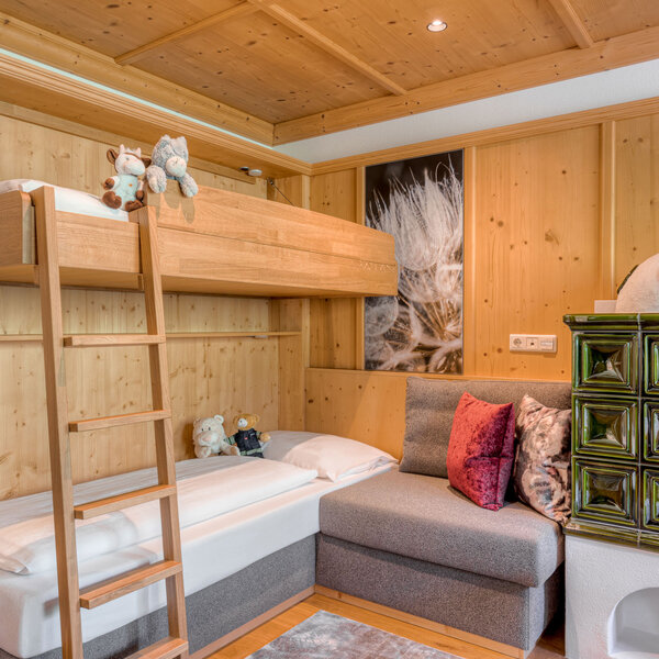 Ein gemütliches Kinderzimmer mit einem Hochbett, einer Treppe und einem Sofa, umgeben von warmem Holz und Spielzeugbären.