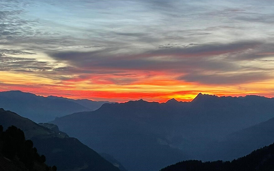 Ein atemberaubender Sonnenaufgang über den Bergen, mit leuchtenden orangefarbenen und roten Farbtönen am Himmel.