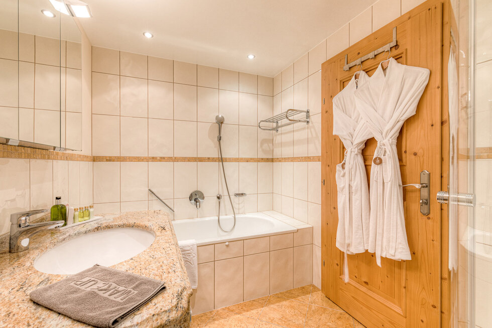 Ein modernes Badezimmer mit einer Badewanne, einem Waschbecken aus Granit und zwei weißen Bademänteln an der Holztür.