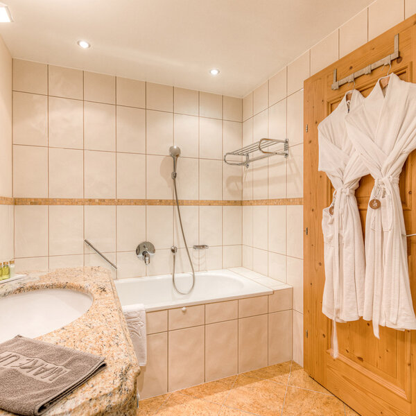 Ein modernes Badezimmer mit einer Badewanne, einem Waschbecken aus Granit und zwei weißen Bademänteln an der Holztür.