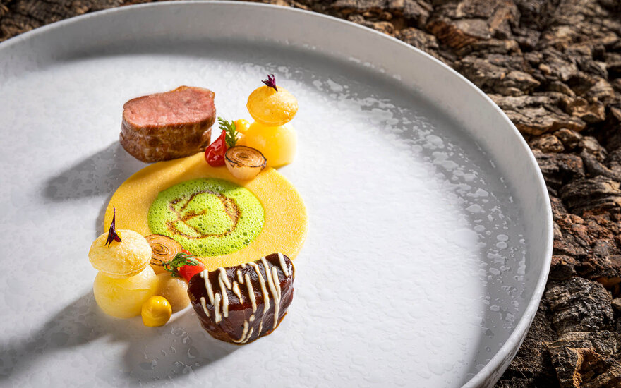 Ein kunstvoll angerichteter Teller mit zartem Fleisch, bunten Beilagen und einer grünen Sauce, die das Gericht lebendig macht.