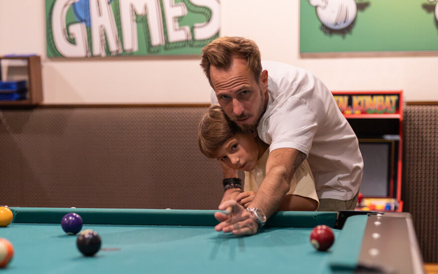 Ein Vater hilft seinem Sohn beim Billiard spielen.