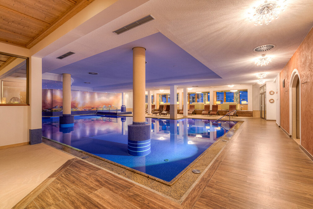 Ein eleganter Innenpool mit blauen Fliesen und sanftem Licht, umgeben von gemütlichen Liegen und großen Fenstern.