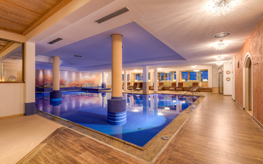 Ein eleganter Innenpool mit blauen Fliesen und sanftem Licht, umgeben von gemütlichen Liegen und großen Fenstern.