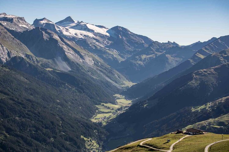 Ein atemberaubender Blick auf die majestätischen Berge und das grüne Tal, das sich unter einem klaren blauen Himmel erstreckt.