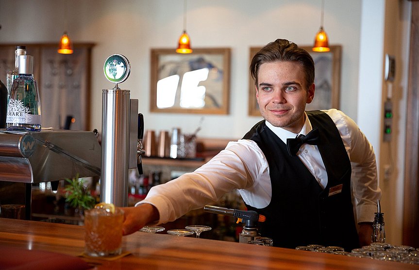 Barmann hinter der Bar stellt einen Cocktail auf die Theke 