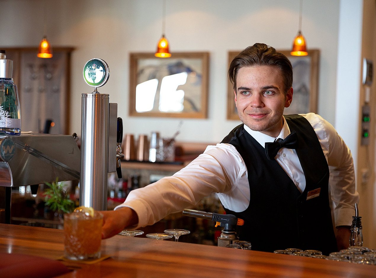 Barmann hinter der Bar stellt einen Cocktail auf die Theke 