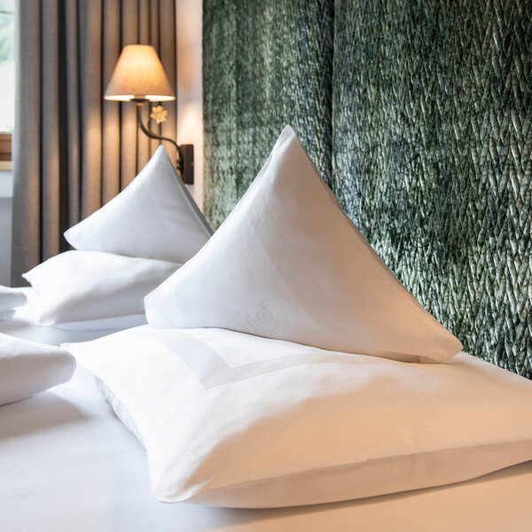 Zwei elegante, spitz zulaufende Kissen liegen auf einem frisch bezogenen Bett in einem stilvollen Schlafzimmer.