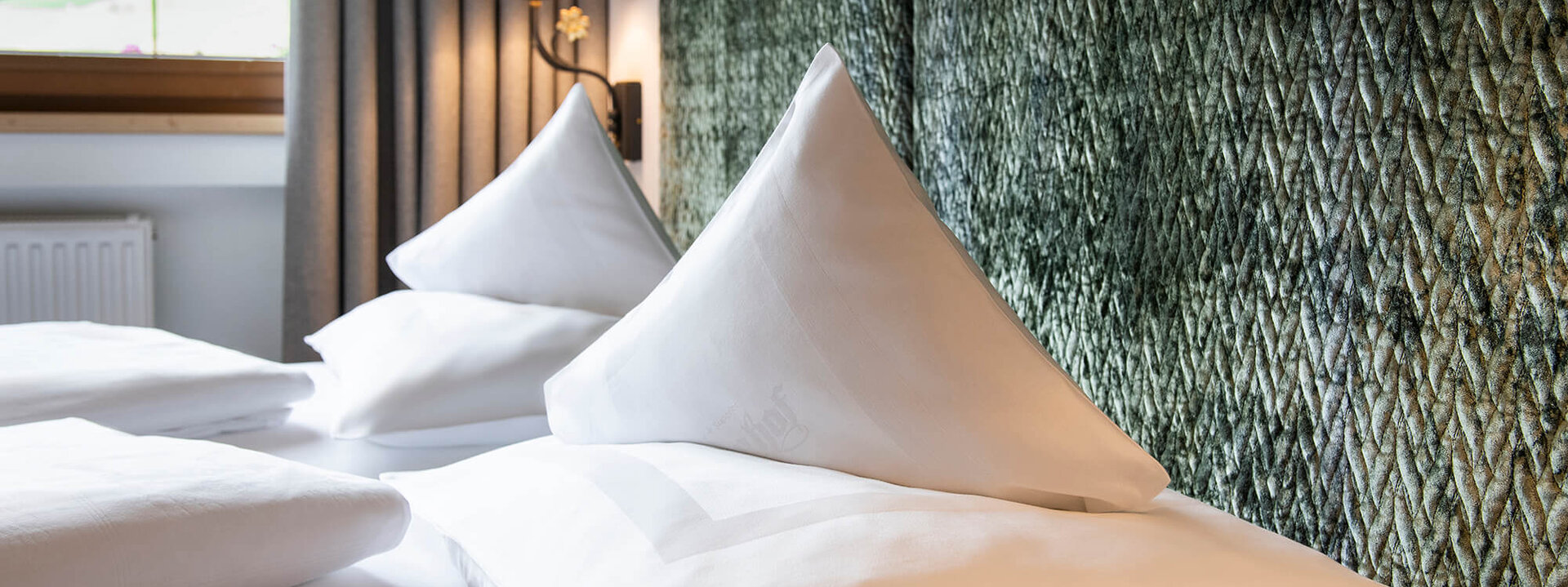 Zwei elegante, spitz zulaufende Kissen liegen auf einem frisch bezogenen Bett in einem stilvollen Schlafzimmer.